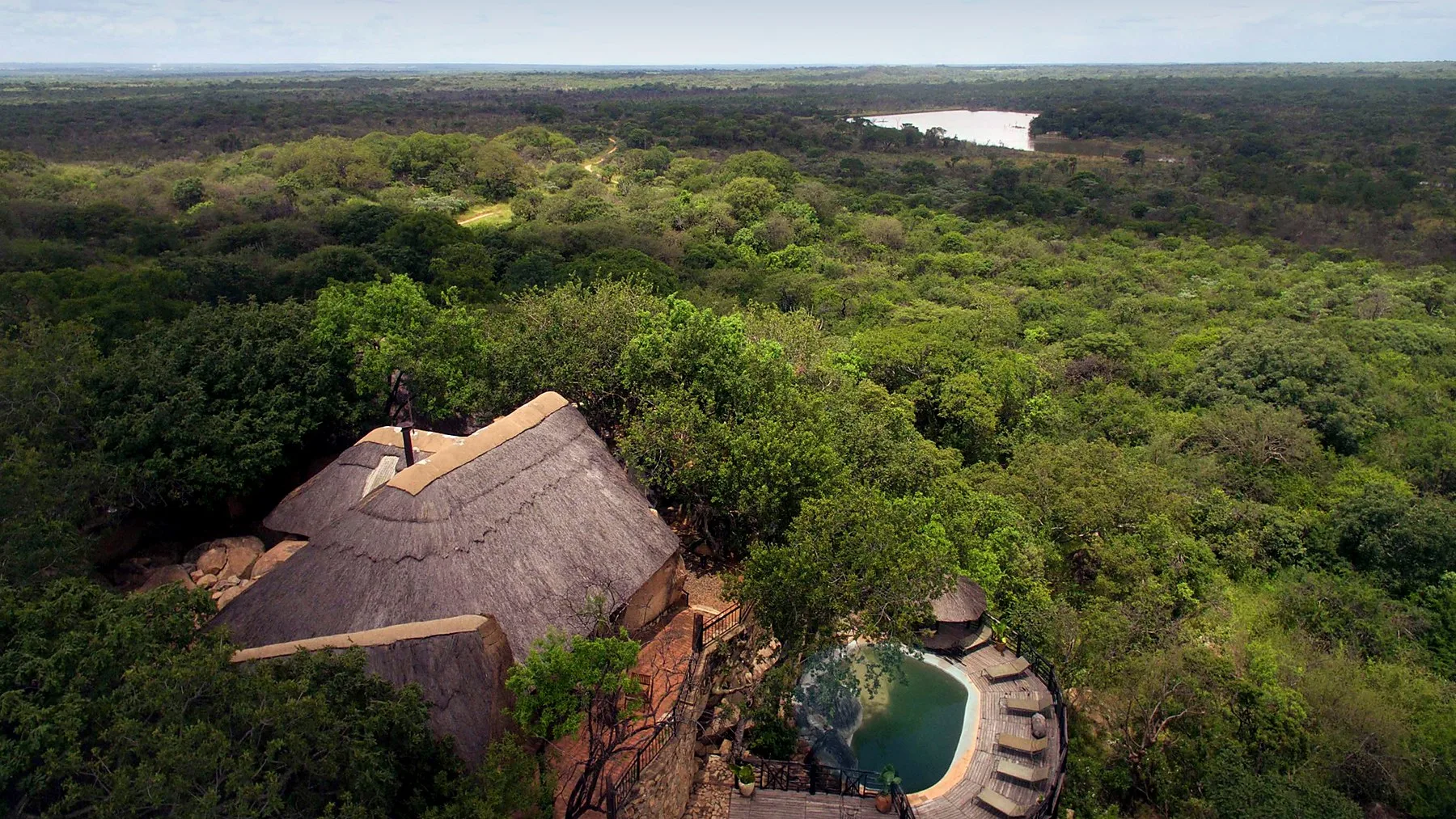 Khami Lodge and its pool from above, thatched roofs set among granite and trees