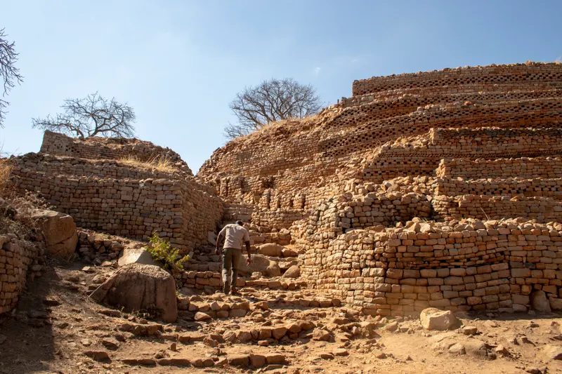 A guide walking up the terraced stone hill at Khami Ruins